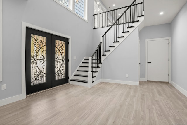 entryway featuring french doors, a towering ceiling, and light hardwood / wood-style flooring