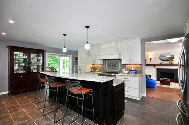 kitchen with white cabinets, a center island with sink, appliances with stainless steel finishes, light stone countertops, and decorative light fixtures