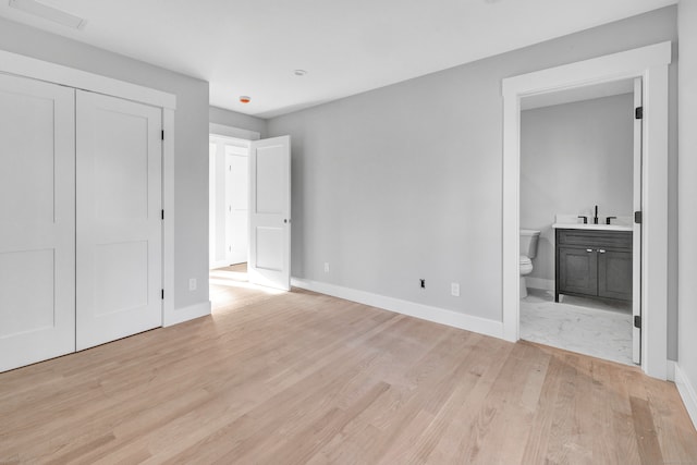 unfurnished bedroom featuring connected bathroom, a closet, sink, and light wood-type flooring