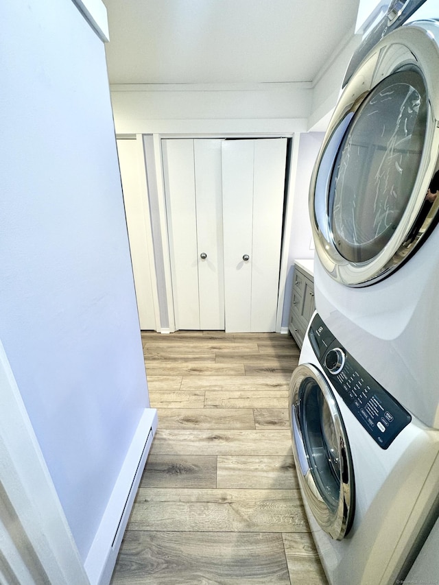 washroom with laundry area, light wood-style flooring, stacked washing maching and dryer, and baseboard heating