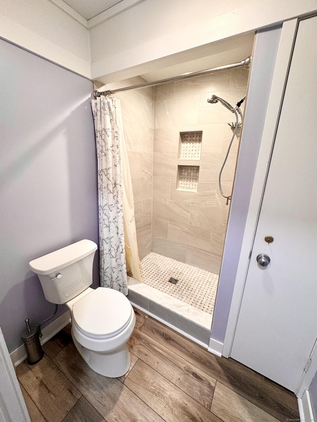 full bath with toilet, wood finished floors, and a stall shower