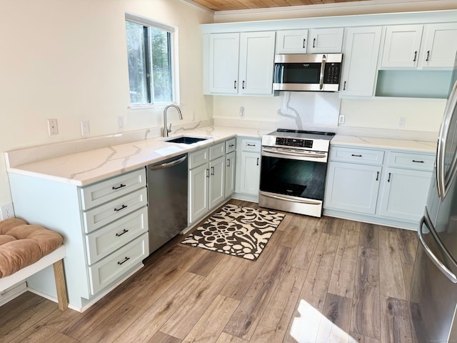 kitchen featuring stainless steel appliances, light stone counters, a sink, and light wood-style flooring
