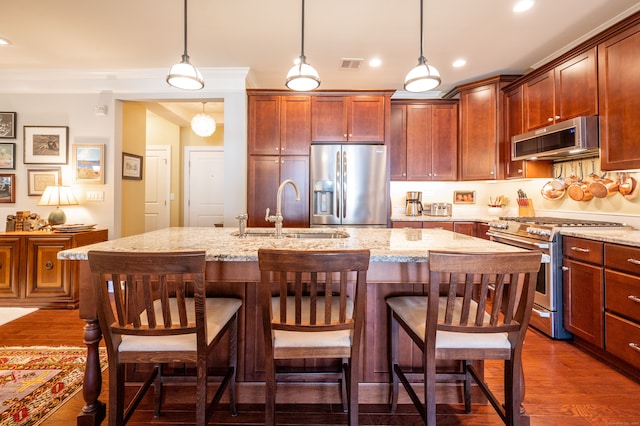 kitchen with appliances with stainless steel finishes, a kitchen island with sink, sink, and dark hardwood / wood-style flooring