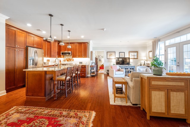 kitchen with appliances with stainless steel finishes, an island with sink, a kitchen bar, hanging light fixtures, and dark wood-type flooring