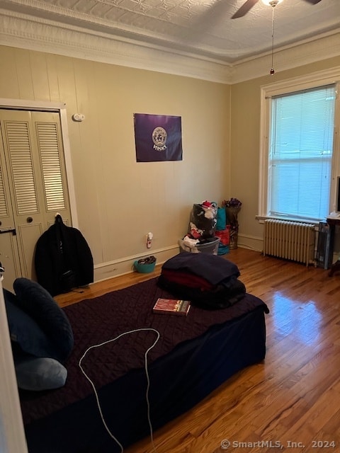 bedroom with radiator heating unit, hardwood / wood-style flooring, ornamental molding, ceiling fan, and a closet