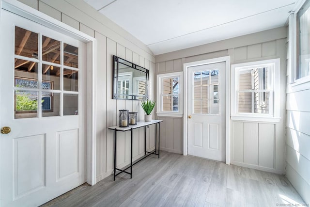 foyer entrance with vaulted ceiling, light hardwood / wood-style floors, a healthy amount of sunlight, and wood walls