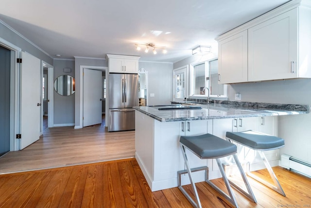 kitchen with white cabinetry, kitchen peninsula, light hardwood / wood-style floors, and stainless steel refrigerator