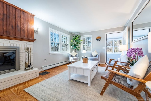 living room with light hardwood / wood-style floors, baseboard heating, and a brick fireplace