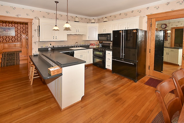 kitchen with black appliances, white cabinetry, pendant lighting, and hardwood / wood-style flooring