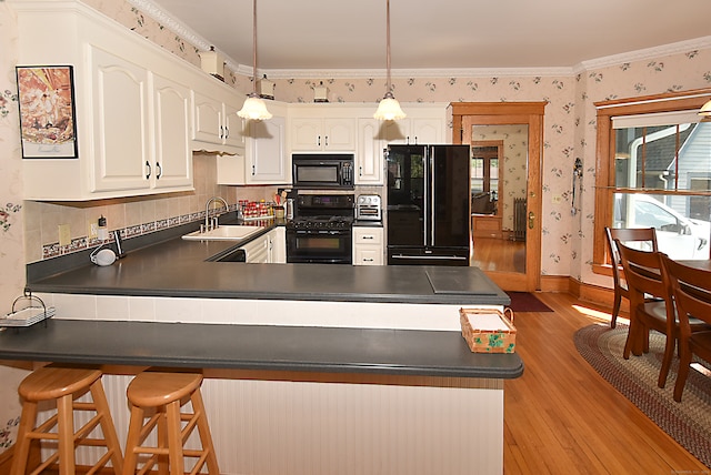 kitchen with kitchen peninsula, hanging light fixtures, white cabinetry, light hardwood / wood-style flooring, and black appliances