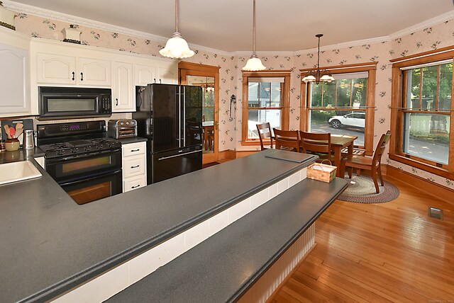 kitchen featuring light hardwood / wood-style floors, white cabinets, black appliances, and pendant lighting