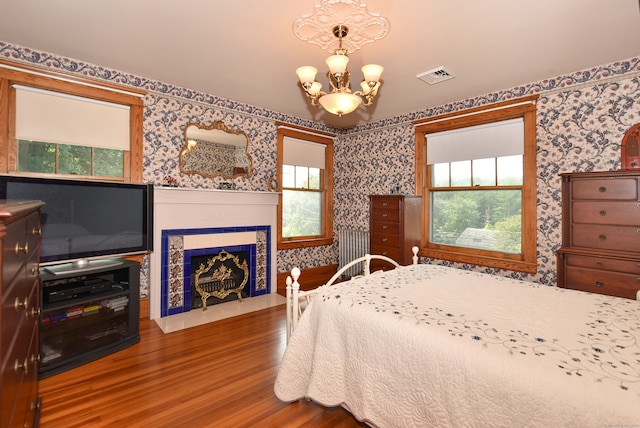 bedroom featuring an inviting chandelier, multiple windows, hardwood / wood-style flooring, and a tiled fireplace