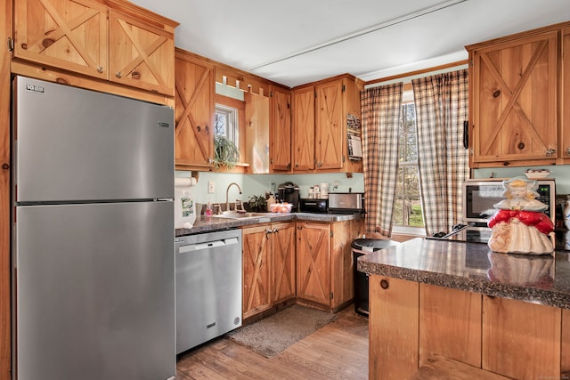 kitchen with kitchen peninsula, stainless steel appliances, dark stone countertops, sink, and light hardwood / wood-style floors