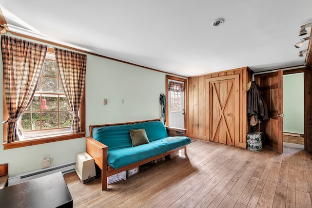 sitting room featuring baseboard heating, crown molding, light hardwood / wood-style floors, and wooden walls