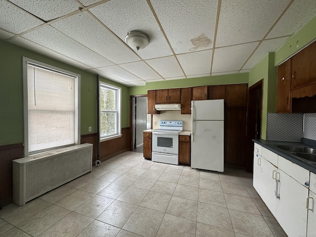 kitchen with sink, white appliances, light tile patterned floors, a paneled ceiling, and radiator heating unit