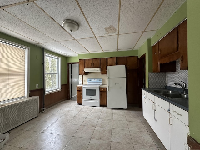 kitchen featuring radiator, sink, light tile patterned floors, a drop ceiling, and white appliances