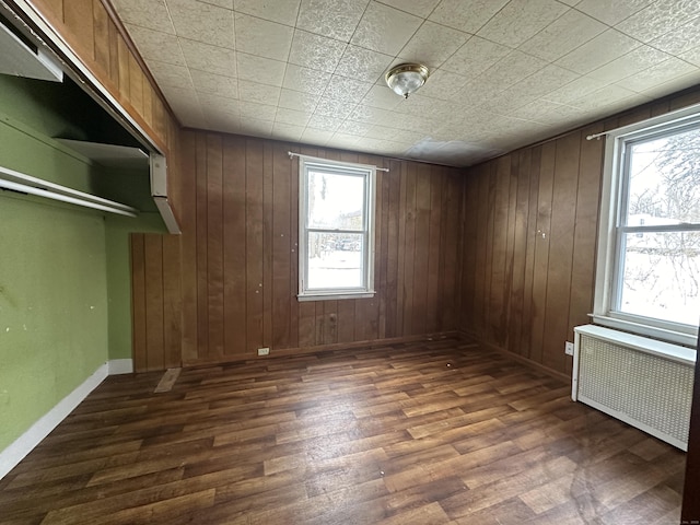 spare room featuring dark wood-type flooring, radiator, and wood walls