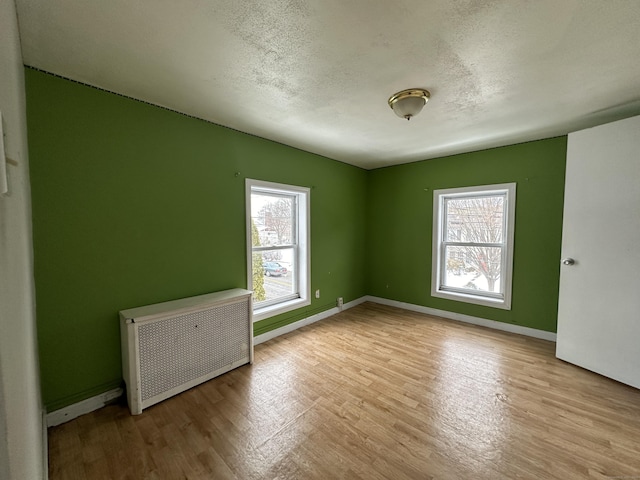 spare room featuring radiator heating unit, a textured ceiling, and light hardwood / wood-style floors