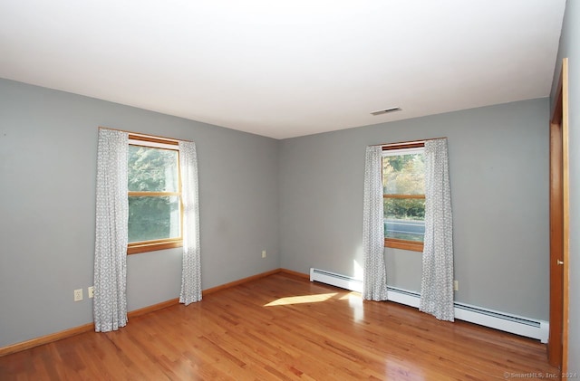 empty room with plenty of natural light, a baseboard radiator, and light hardwood / wood-style flooring