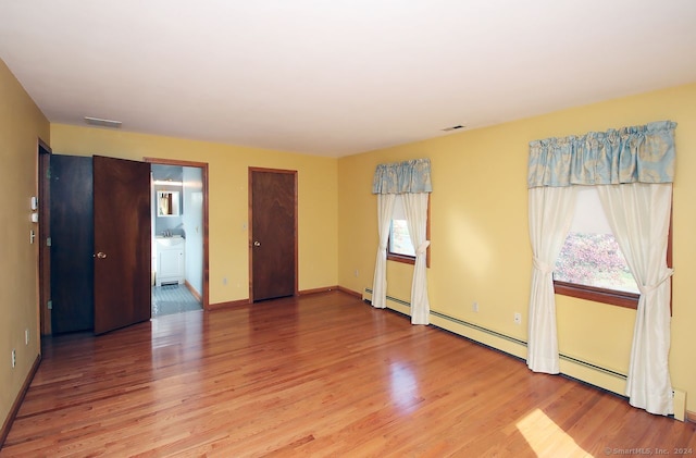 empty room featuring sink, wood-type flooring, and a baseboard radiator