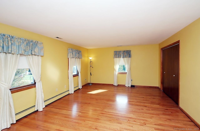 unfurnished room featuring a wealth of natural light, light hardwood / wood-style flooring, and a baseboard radiator