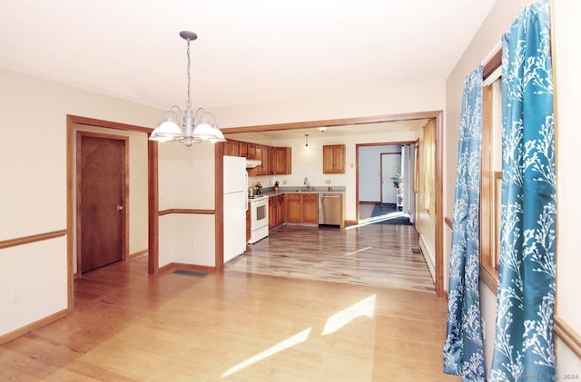 kitchen with light wood-type flooring, white appliances, sink, a chandelier, and hanging light fixtures