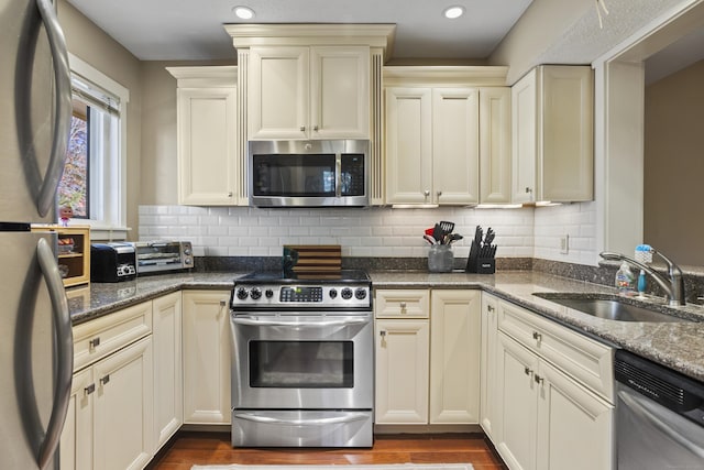 kitchen with appliances with stainless steel finishes, cream cabinets, dark stone counters, and sink