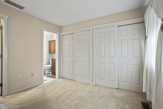 unfurnished bedroom with light carpet, connected bathroom, and two closets