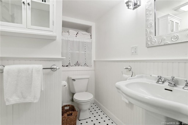 bathroom featuring tile patterned floors, toilet, wooden walls, and sink