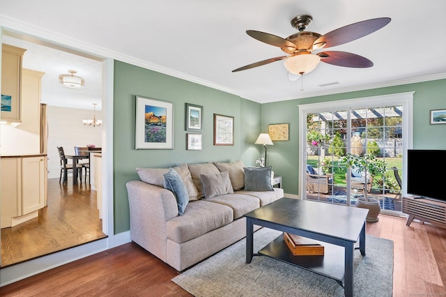 living area with baseboards, ornamental molding, wood finished floors, and ceiling fan with notable chandelier