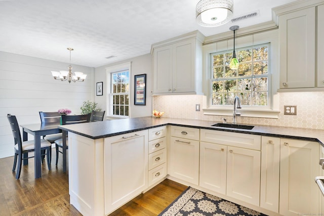 kitchen with a peninsula, a sink, visible vents, dark countertops, and dark wood finished floors