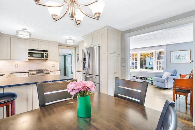 kitchen with a breakfast bar area, a notable chandelier, appliances with stainless steel finishes, decorative backsplash, and dark countertops