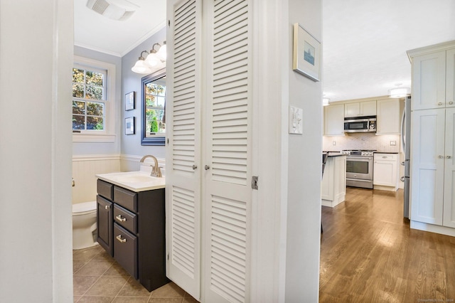 bathroom featuring visible vents, decorative backsplash, toilet, a wainscoted wall, and crown molding