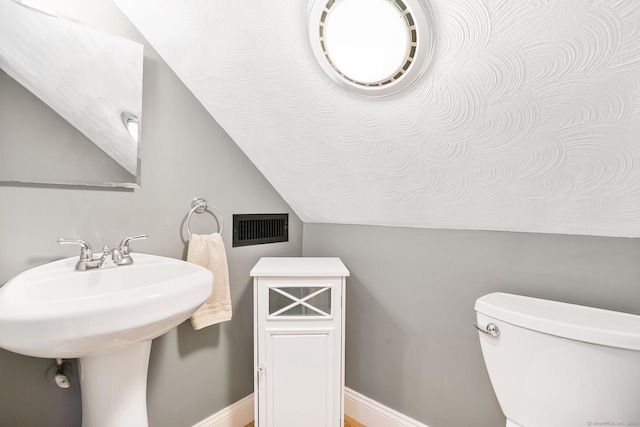 bathroom with lofted ceiling, toilet, a sink, visible vents, and baseboards