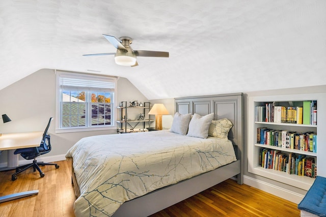 bedroom with lofted ceiling, a textured ceiling, baseboards, and wood finished floors