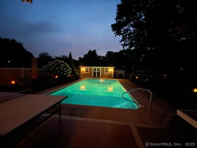 pool at dusk featuring a patio area, an outdoor pool, and an outdoor structure