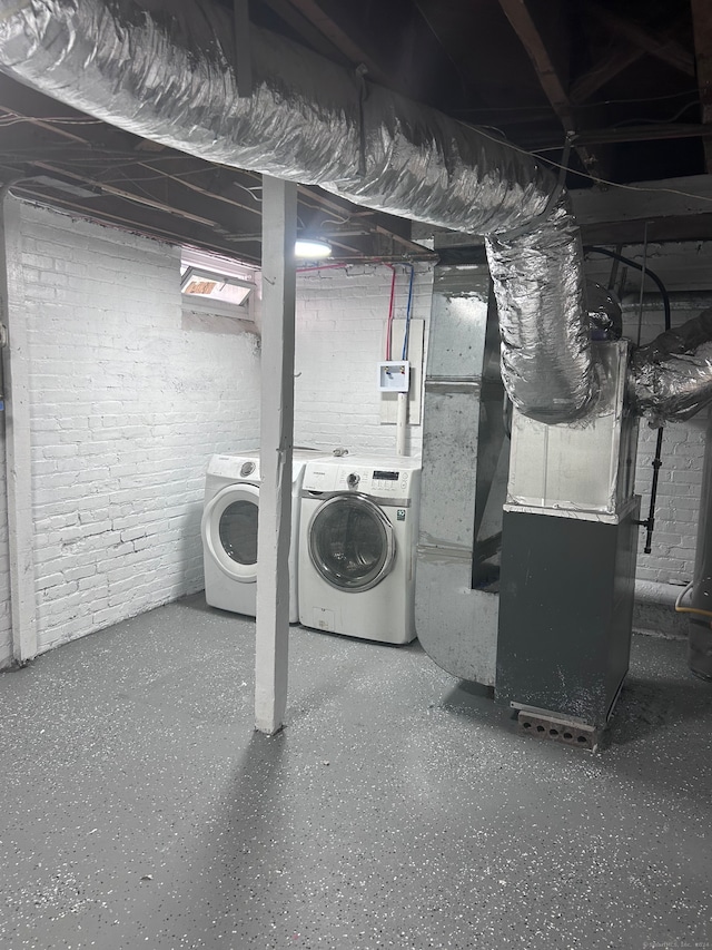 basement featuring brick wall, heating unit, and washer and clothes dryer