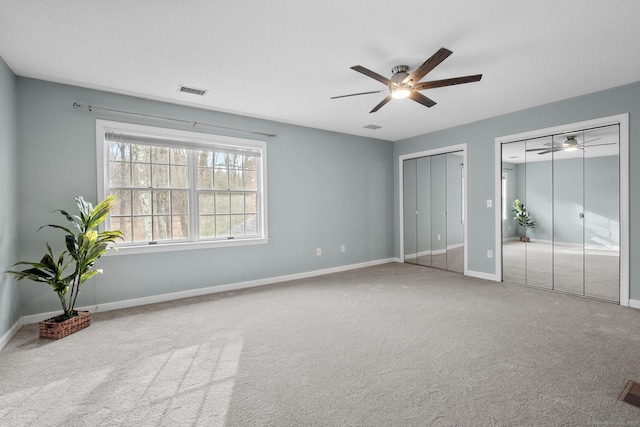 unfurnished bedroom featuring ceiling fan, carpet floors, and multiple closets