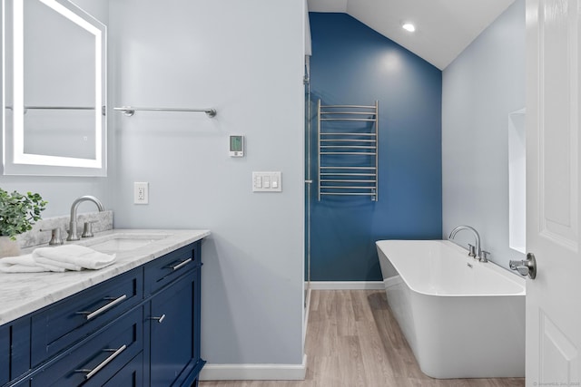 bathroom with radiator heating unit, wood-type flooring, vanity, vaulted ceiling, and a washtub