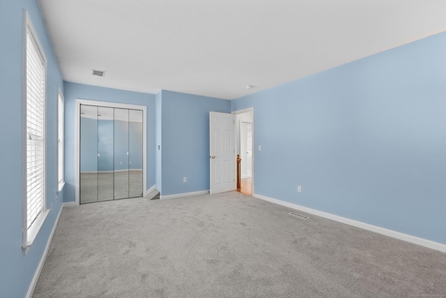 unfurnished bedroom featuring light carpet, a closet, and multiple windows