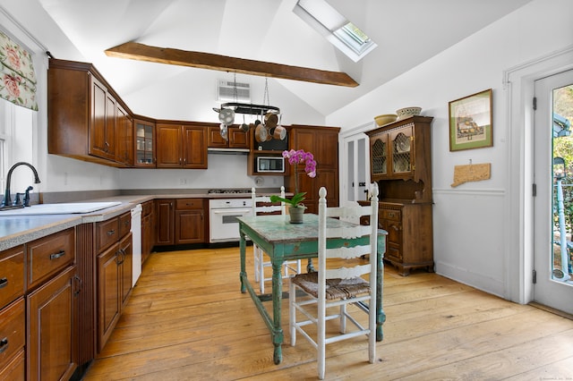 kitchen featuring oven, stainless steel microwave, a skylight, sink, and light hardwood / wood-style flooring