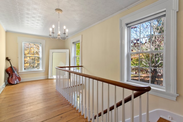 corridor featuring light hardwood / wood-style flooring, crown molding, a wealth of natural light, and an inviting chandelier