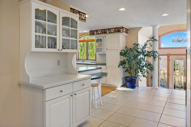 kitchen with light tile patterned floors, backsplash, white cabinetry, and a notable chandelier