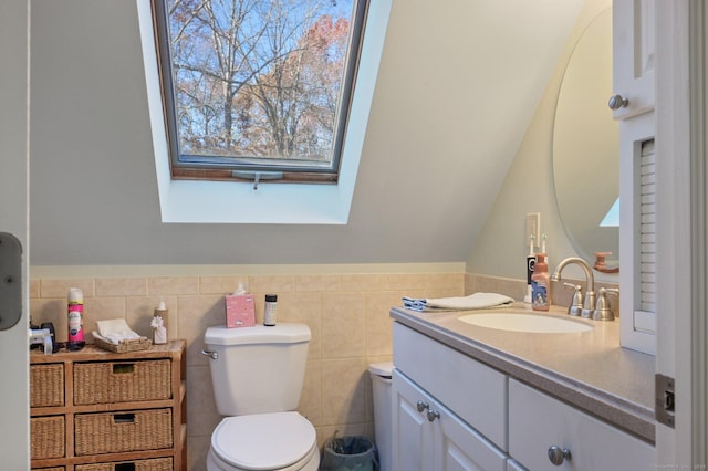 bathroom featuring a skylight, vanity, tile walls, and toilet