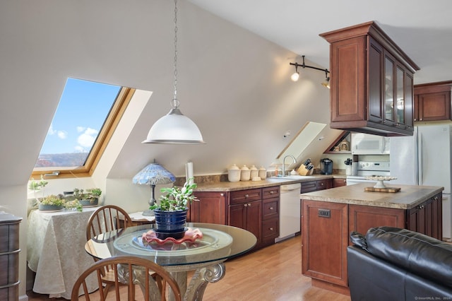 kitchen featuring white appliances, sink, vaulted ceiling with skylight, light wood-type flooring, and decorative light fixtures