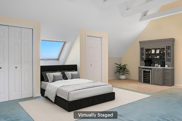 bedroom featuring light carpet, bar area, vaulted ceiling with beams, wine cooler, and multiple closets