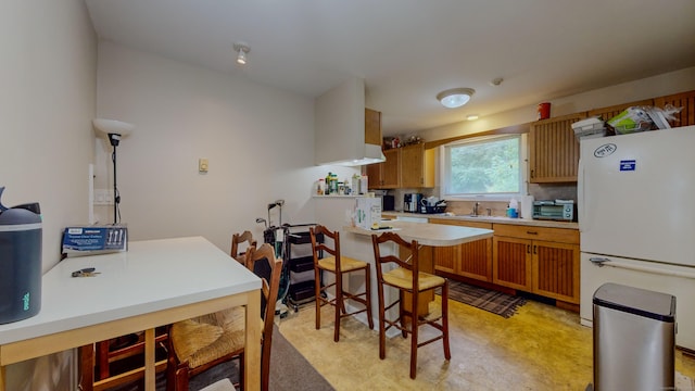 kitchen with a toaster, light countertops, brown cabinetry, freestanding refrigerator, and a sink