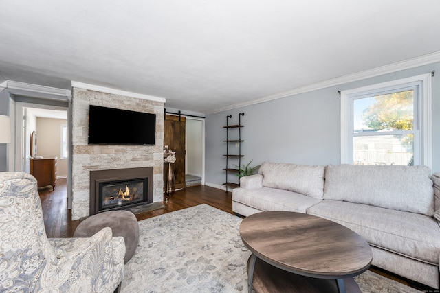 living room with dark hardwood / wood-style flooring, crown molding, a stone fireplace, and a barn door