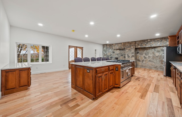 kitchen featuring appliances with stainless steel finishes, light stone counters, light hardwood / wood-style floors, and a center island