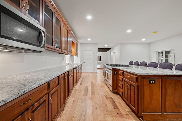 kitchen featuring light stone counters, stainless steel appliances, light wood-type flooring, a kitchen bar, and sink